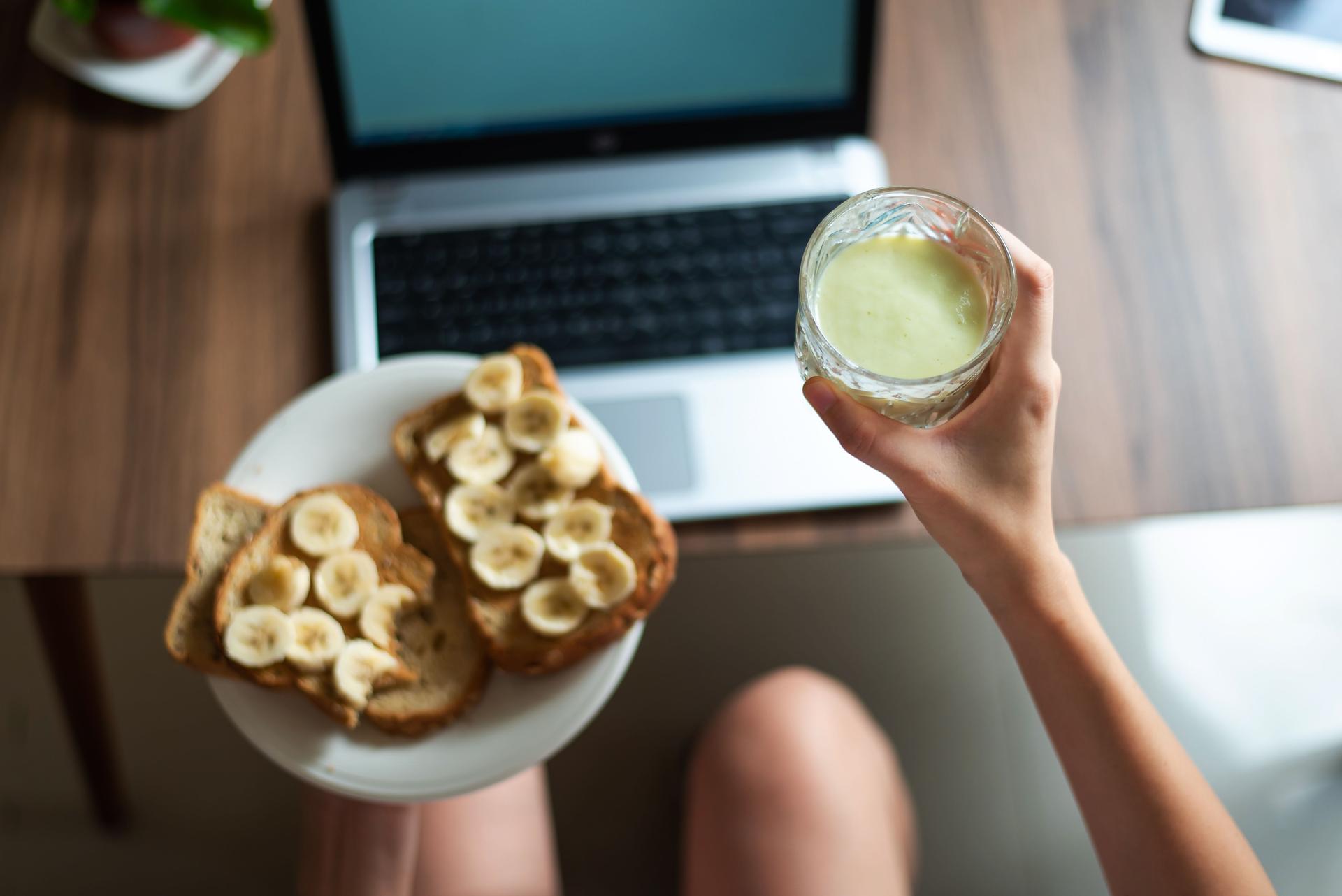 Woman having breakfast while working from the sofa at home first person view