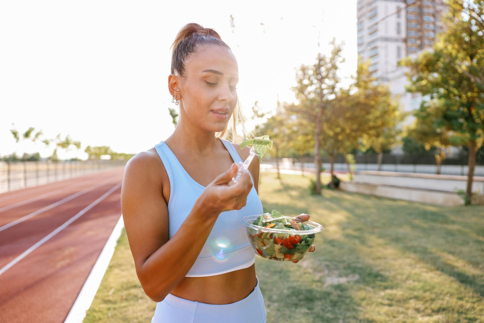 Young woman eating a healthy salad after workout. Fitness and healthy lifestyle concept.